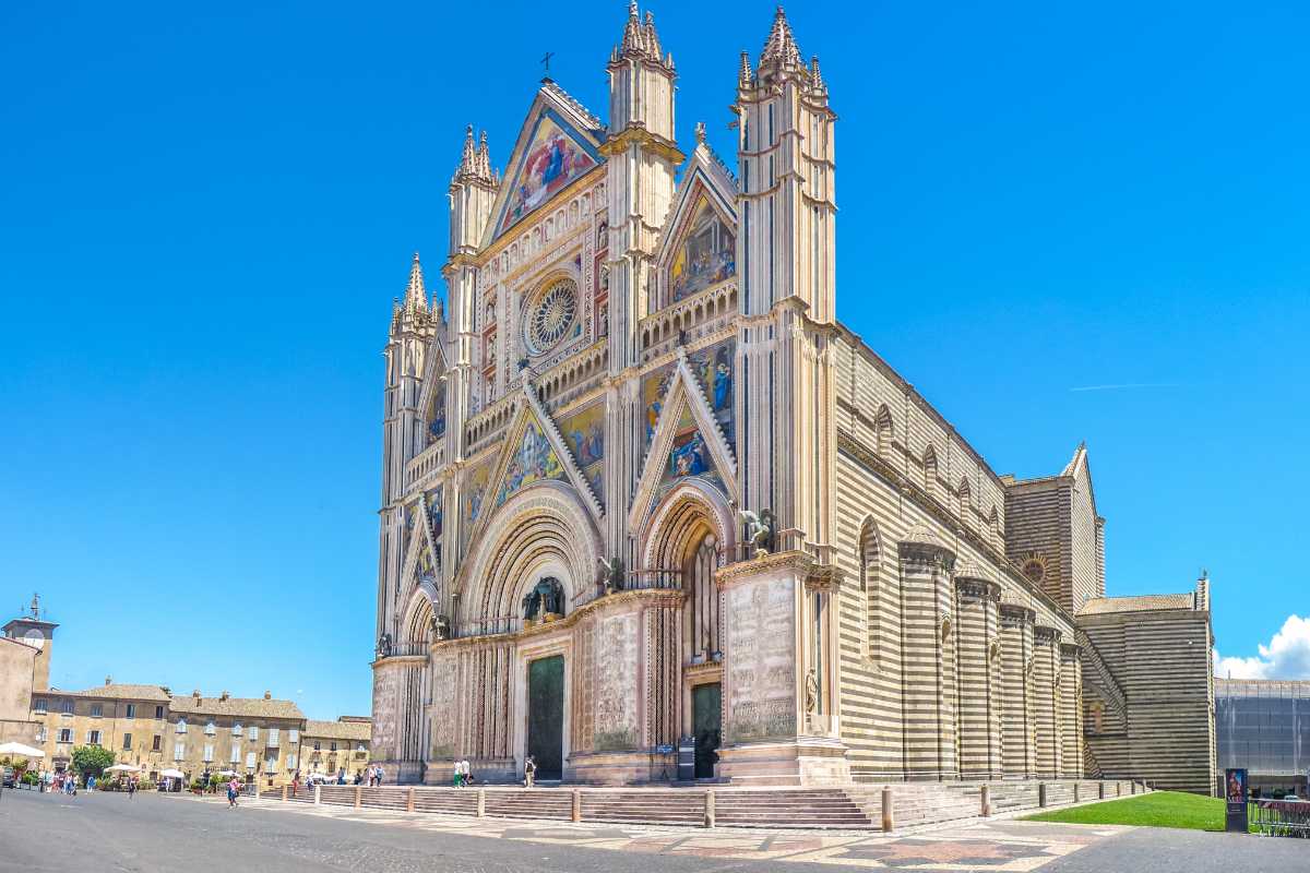 Vista panoramica della città di Orvieto arroccata sulla rupe, con treni e auto che arrivano dalla campagna circostante, atmosfera di viaggio e arrivo
